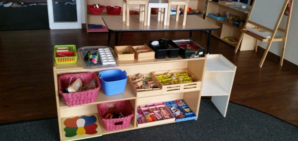 Wooden shelving unit with various bins and items in a classroom