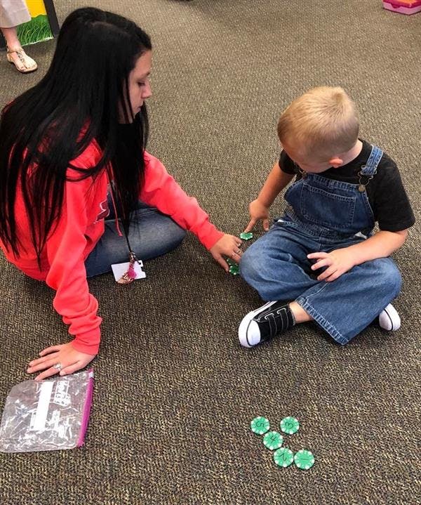Person and child sitting on floor playing with green tokens