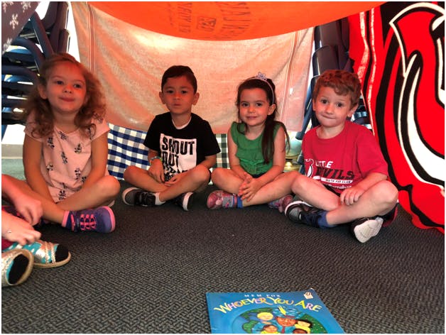 Four children sitting on the floor under a blanket fort
