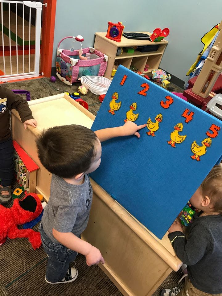 Child pointing at a blue board with numbers and ducks