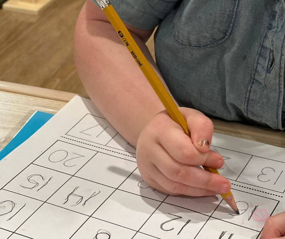 Child's hand holding a pencil and writing numbers on a worksheet