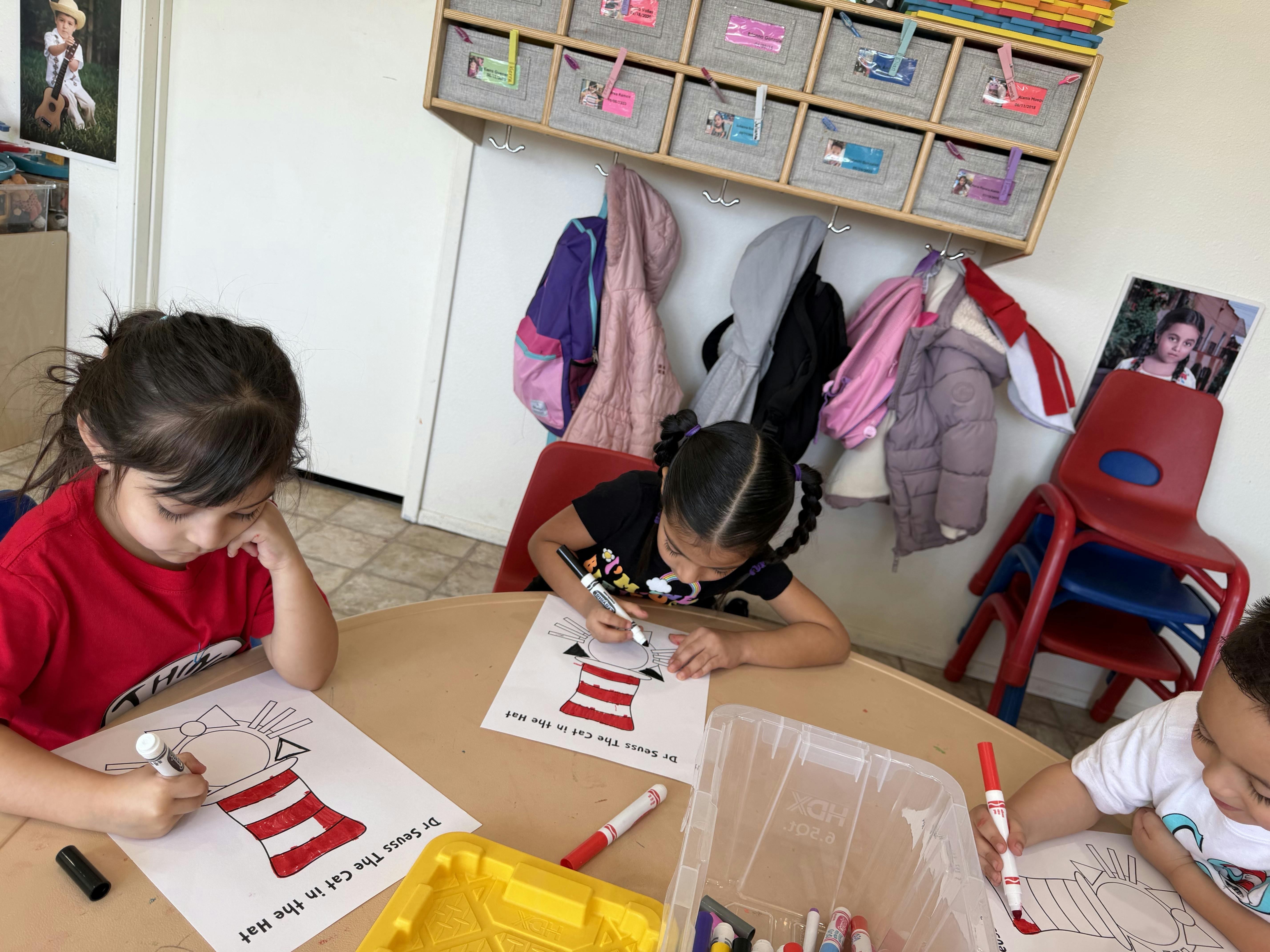 Three children sitting at a table coloring images of Dr Seuss's The Cat in the Hat