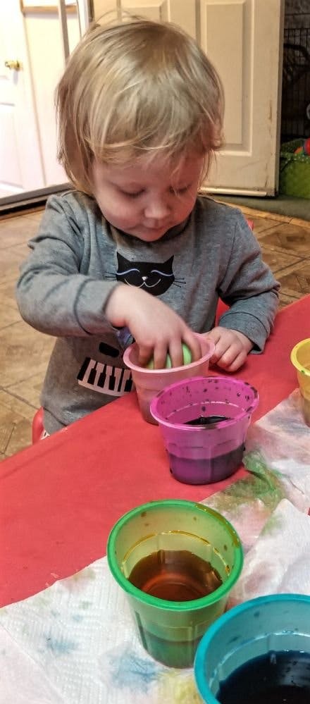 Child dipping an egg into a cup of dye