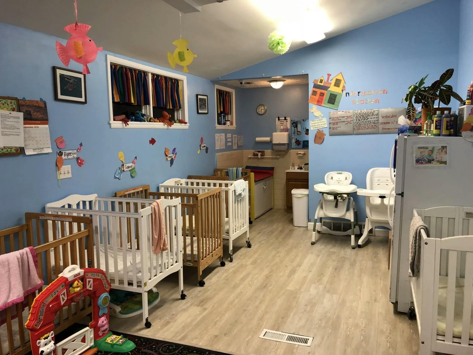 Daycare room with multiple cribs, high chairs, and a play area