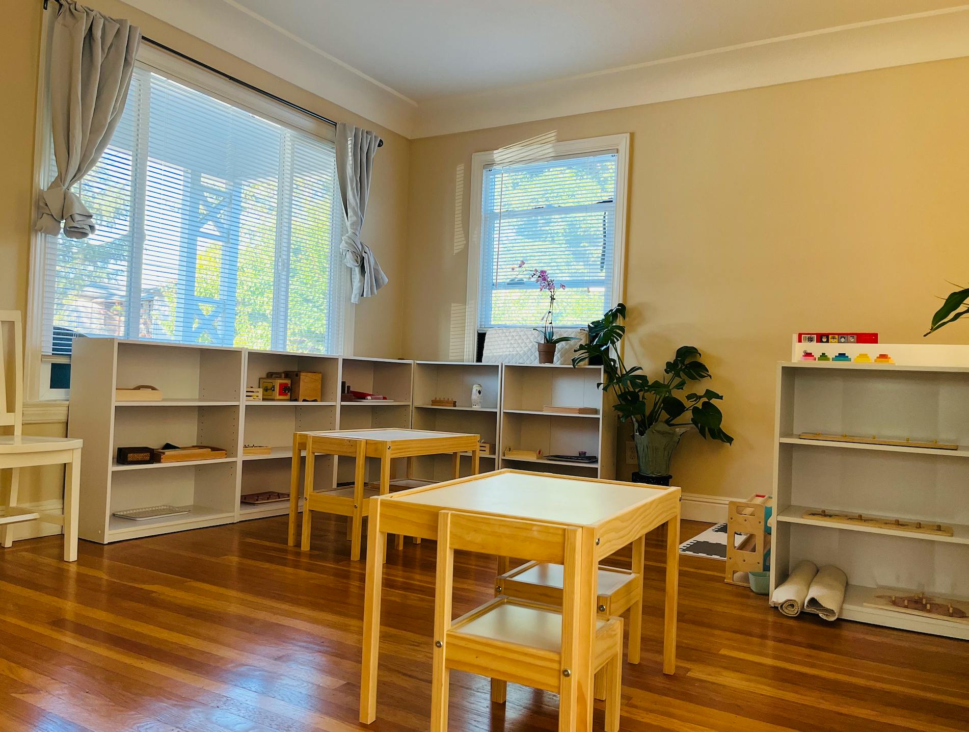 Empty classroom with small tables and chairs, and shelves along the walls