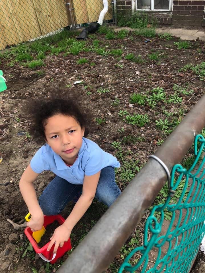 Child kneeling in dirt with a red bucket and yellow shovel