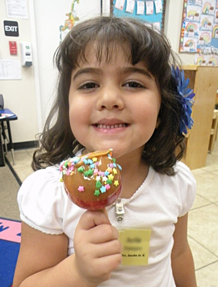 Child holding a caramel apple with sprinkles