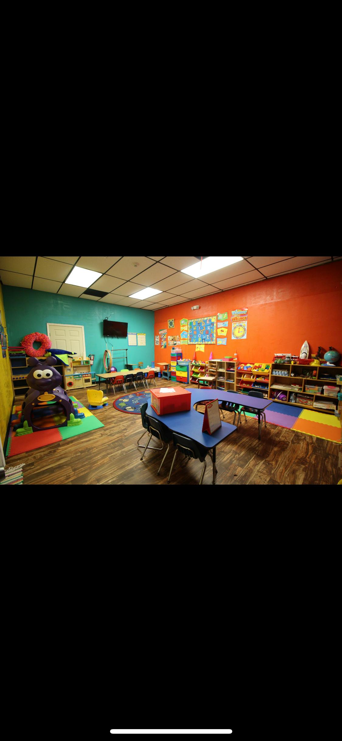 Classroom with colorful walls, small tables, chairs, and shelves with toys