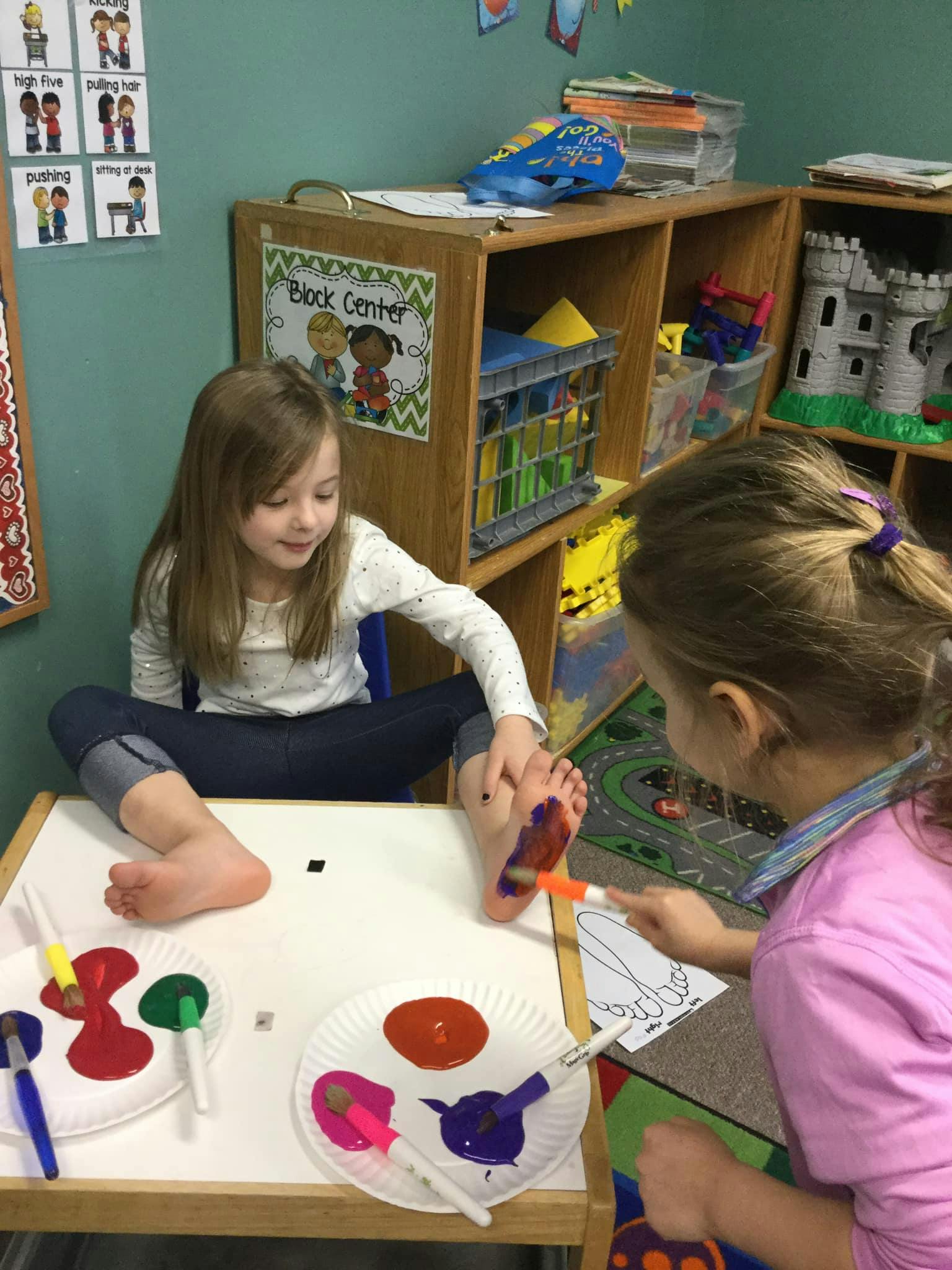 Child painting another child's foot with colorful paint