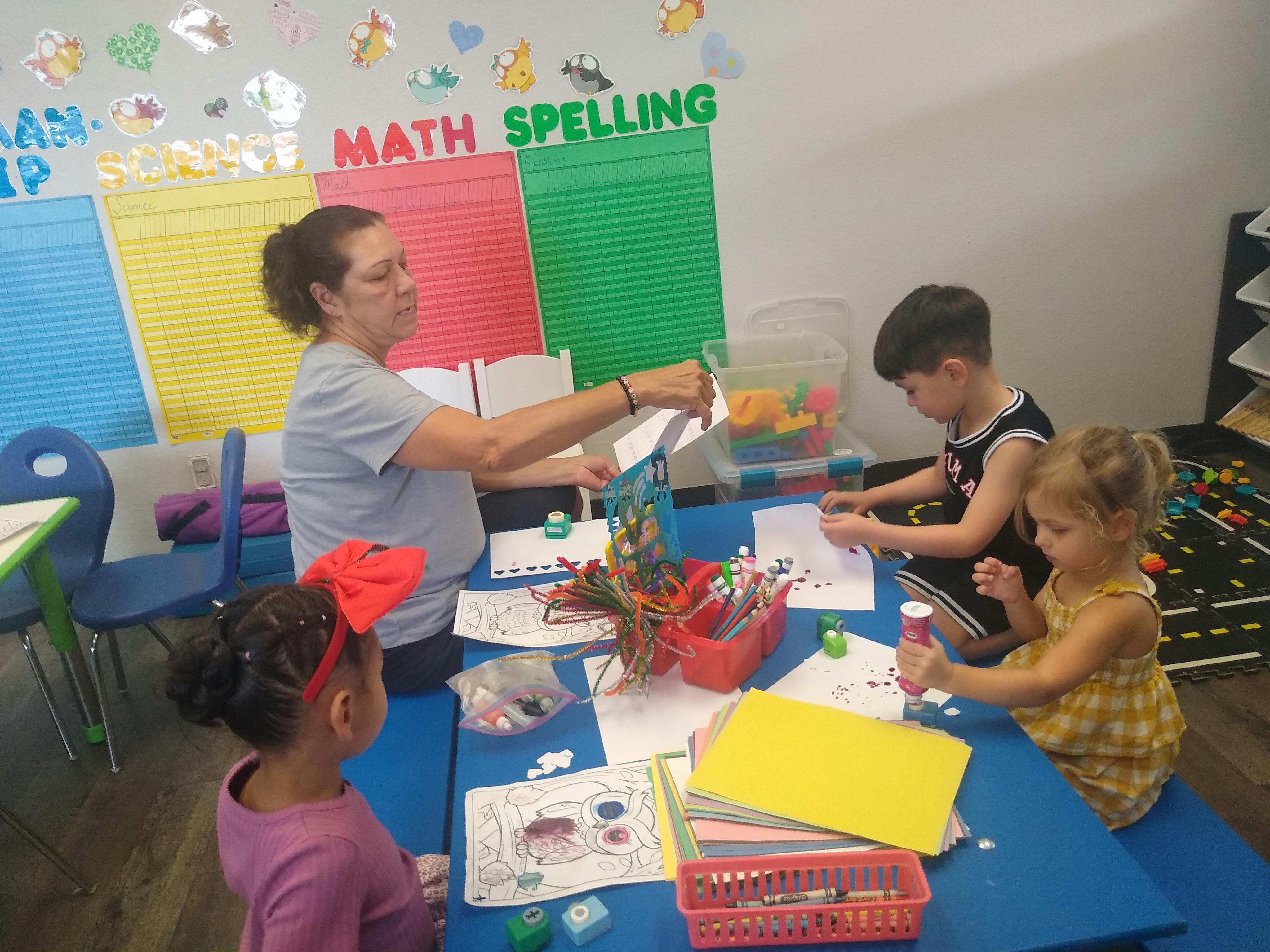 Adult assisting children with art projects at a classroom table