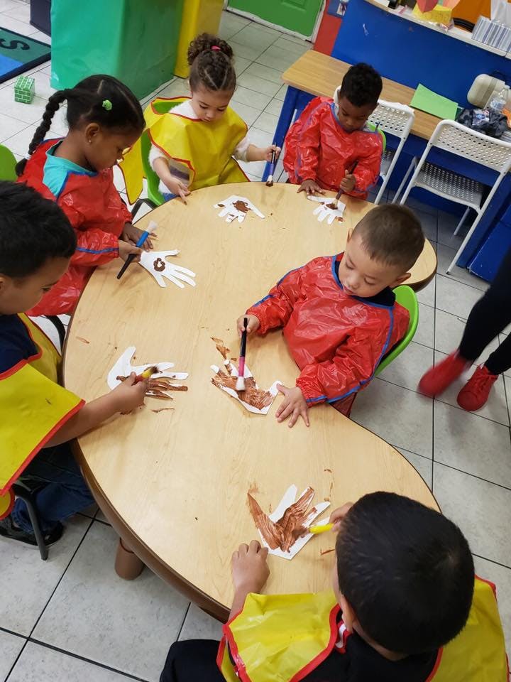 Children painting handprint cutouts at a table