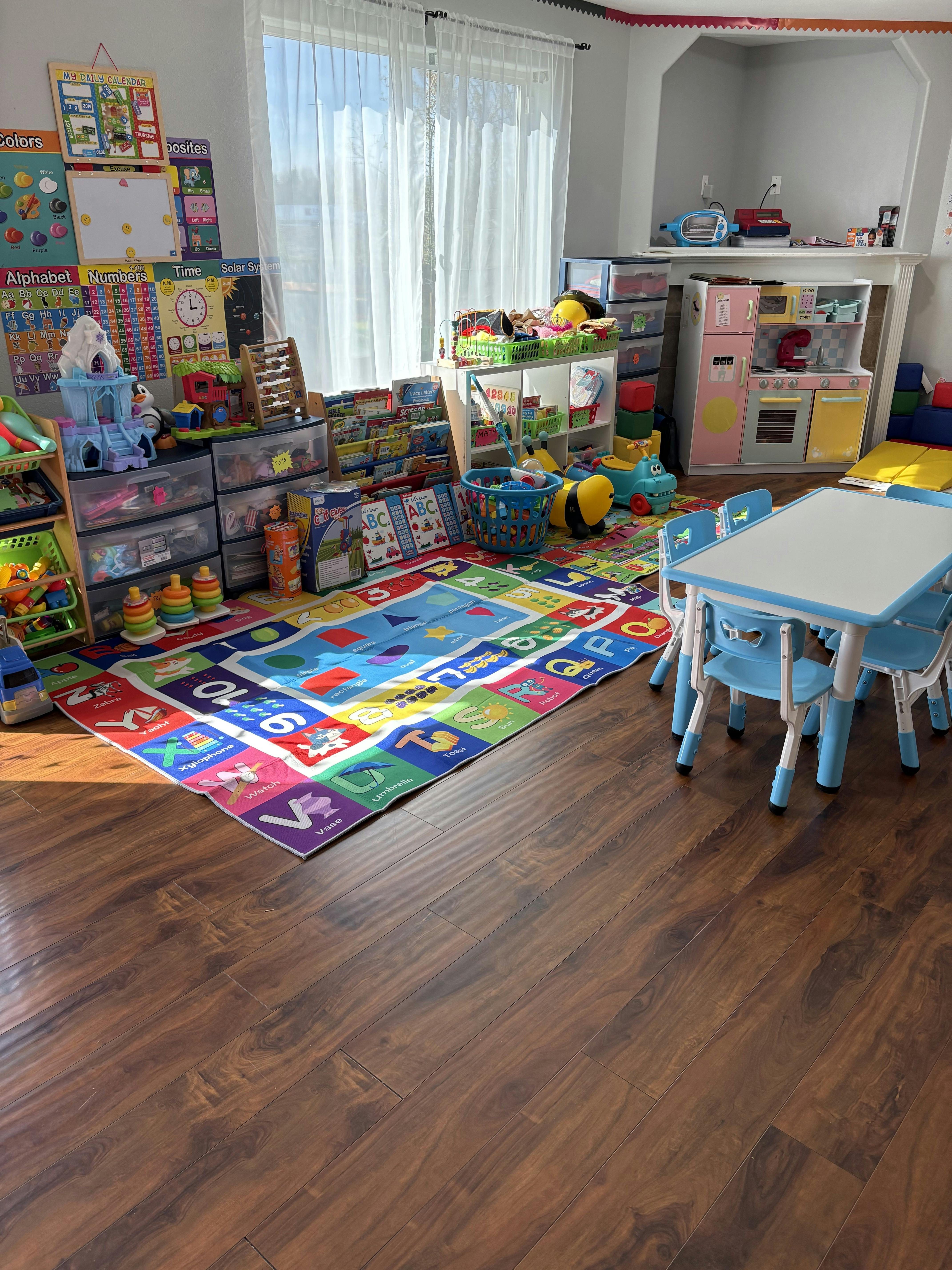 A classroom with a colorful alphabet rug, small blue table and chairs, and various toys