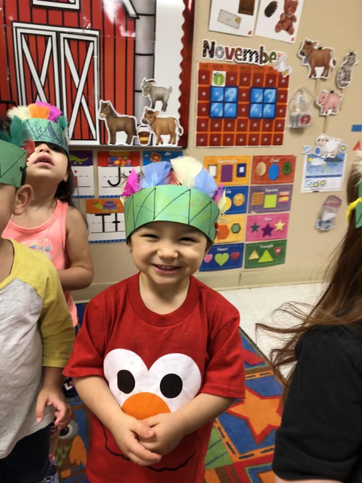 Child in a red shirt and paper hat smiling at the camera