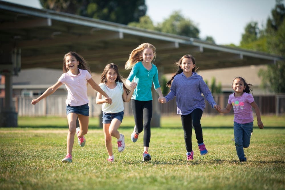 Five children running across a grassy field