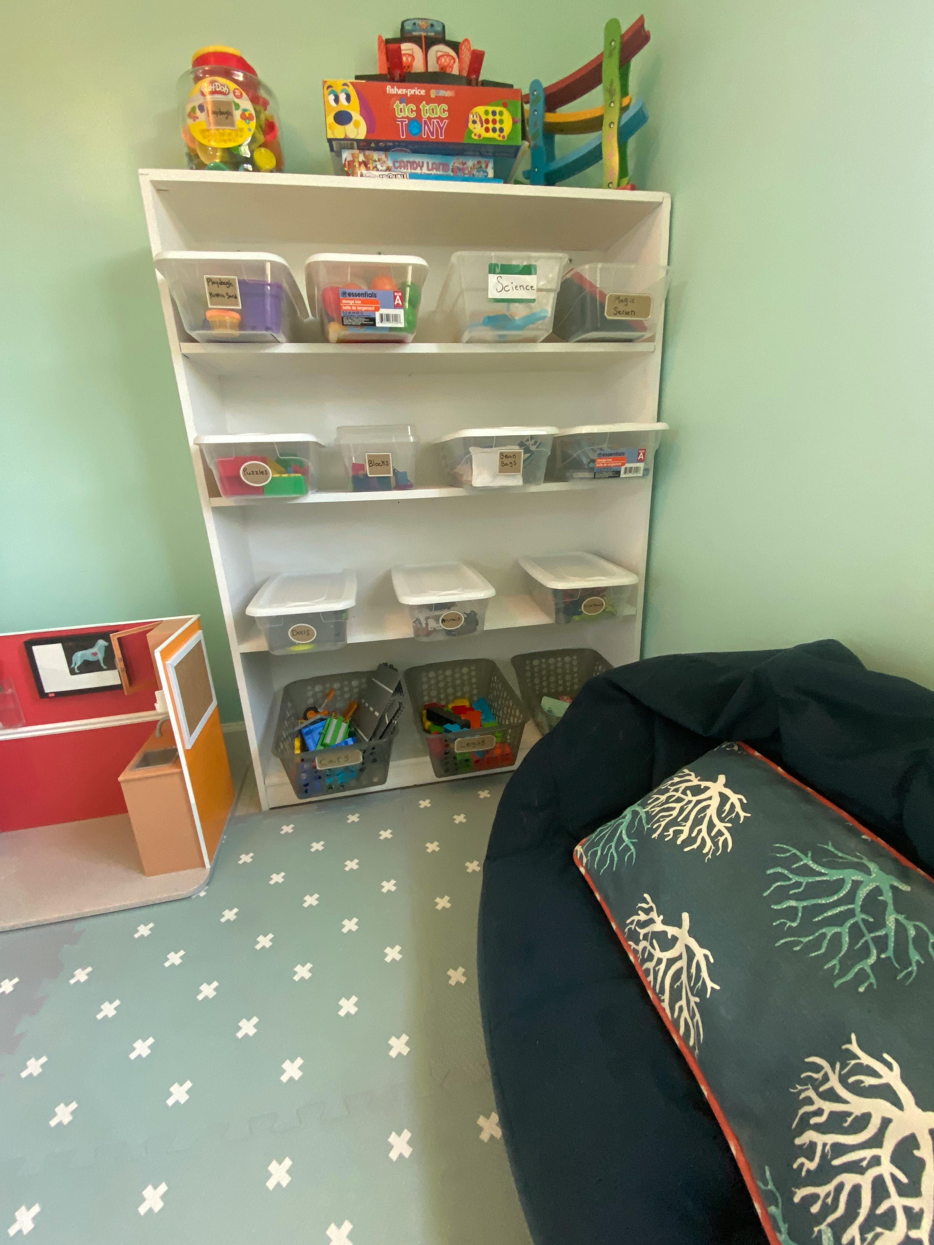 White shelving unit with clear storage bins and toys, next to a beanbag chair