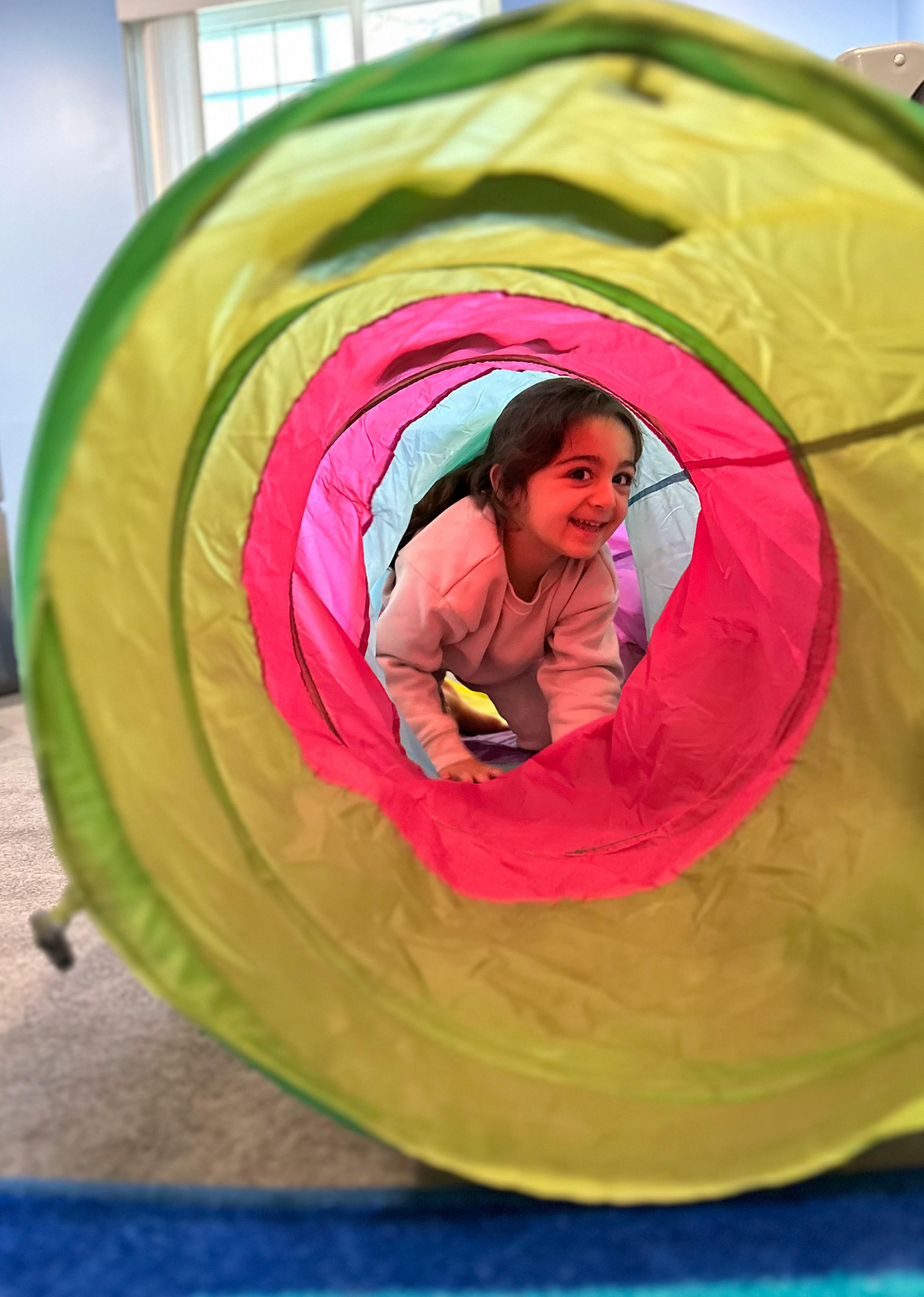 Child crawling through a colorful play tunnel