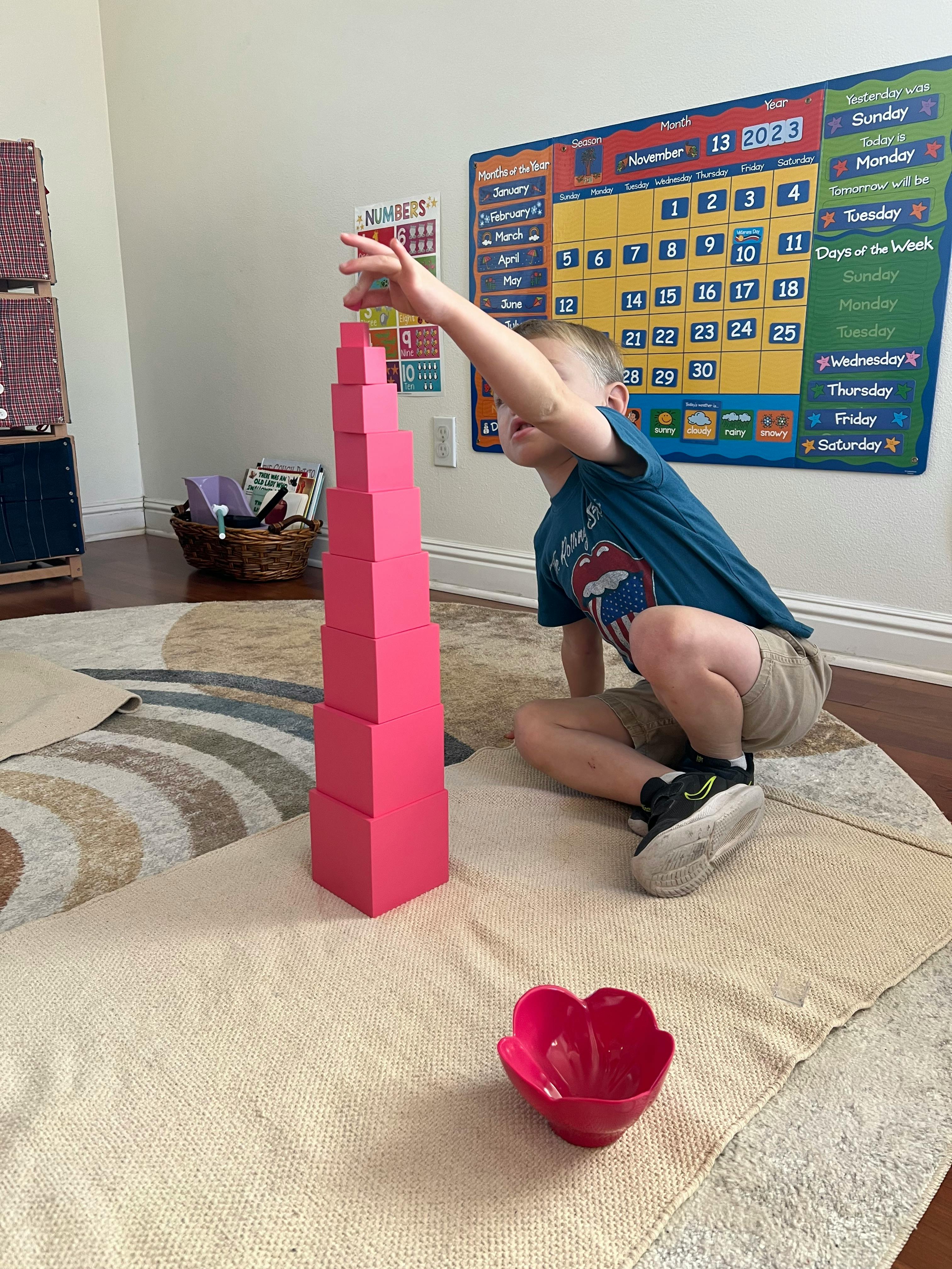 Child reaching for a tall stack of pink blocks