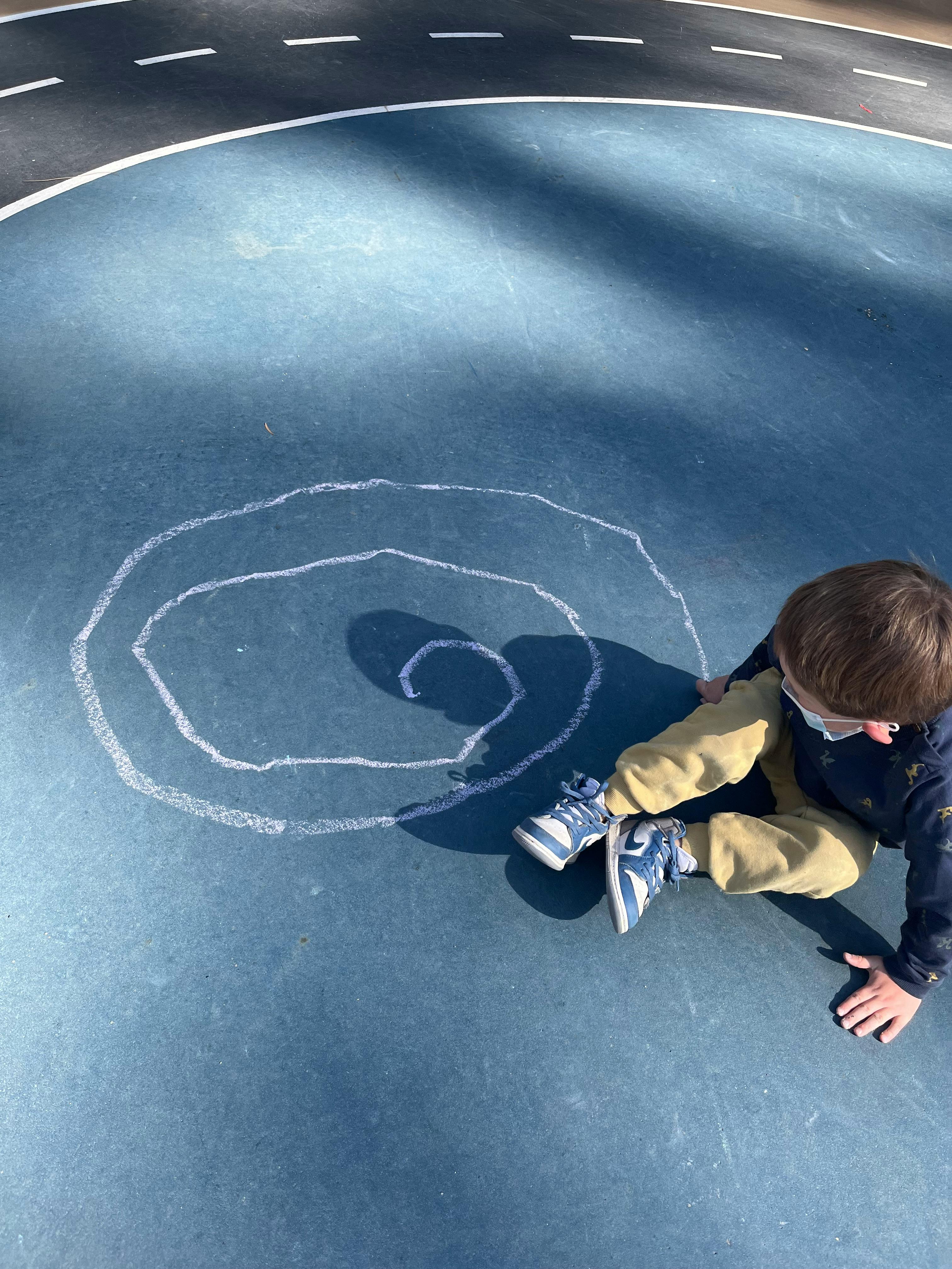 Child sitting on ground next to chalk drawing