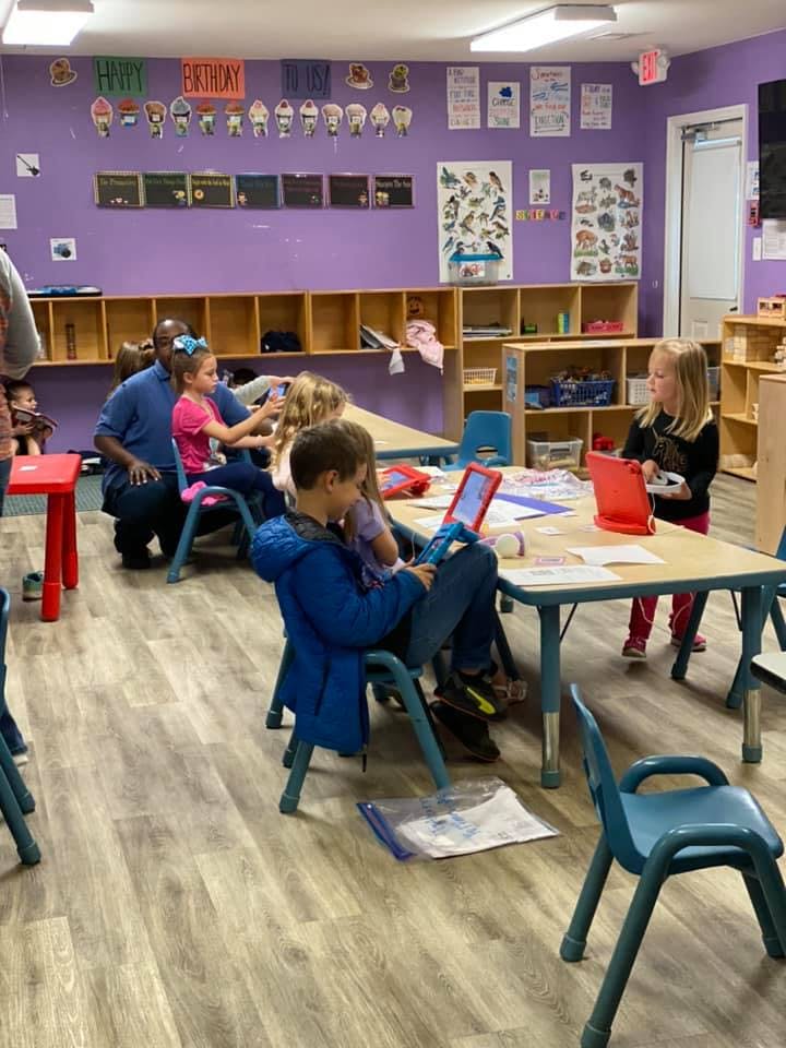 Children and adults in a classroom with tables and chairs
