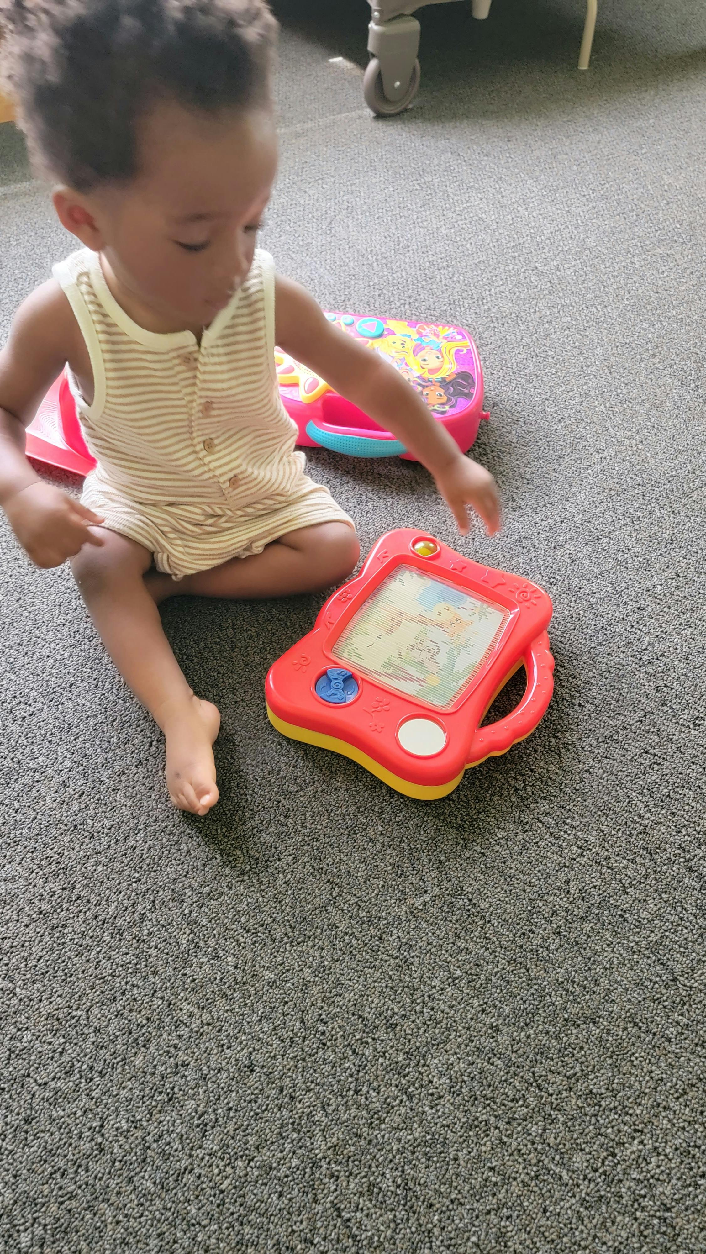 Child sitting on carpet playing with a red drawing toy