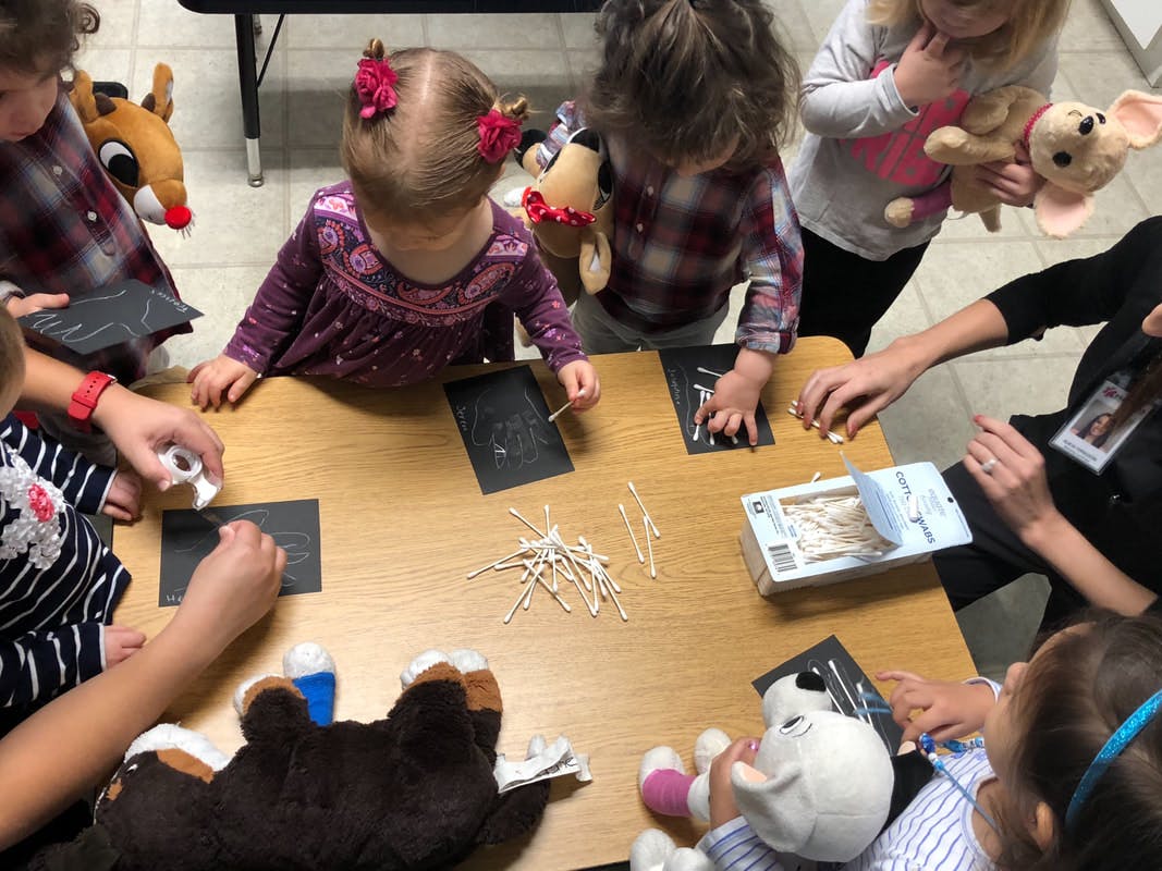 Children and an adult at a table doing an activity with cotton swabs
