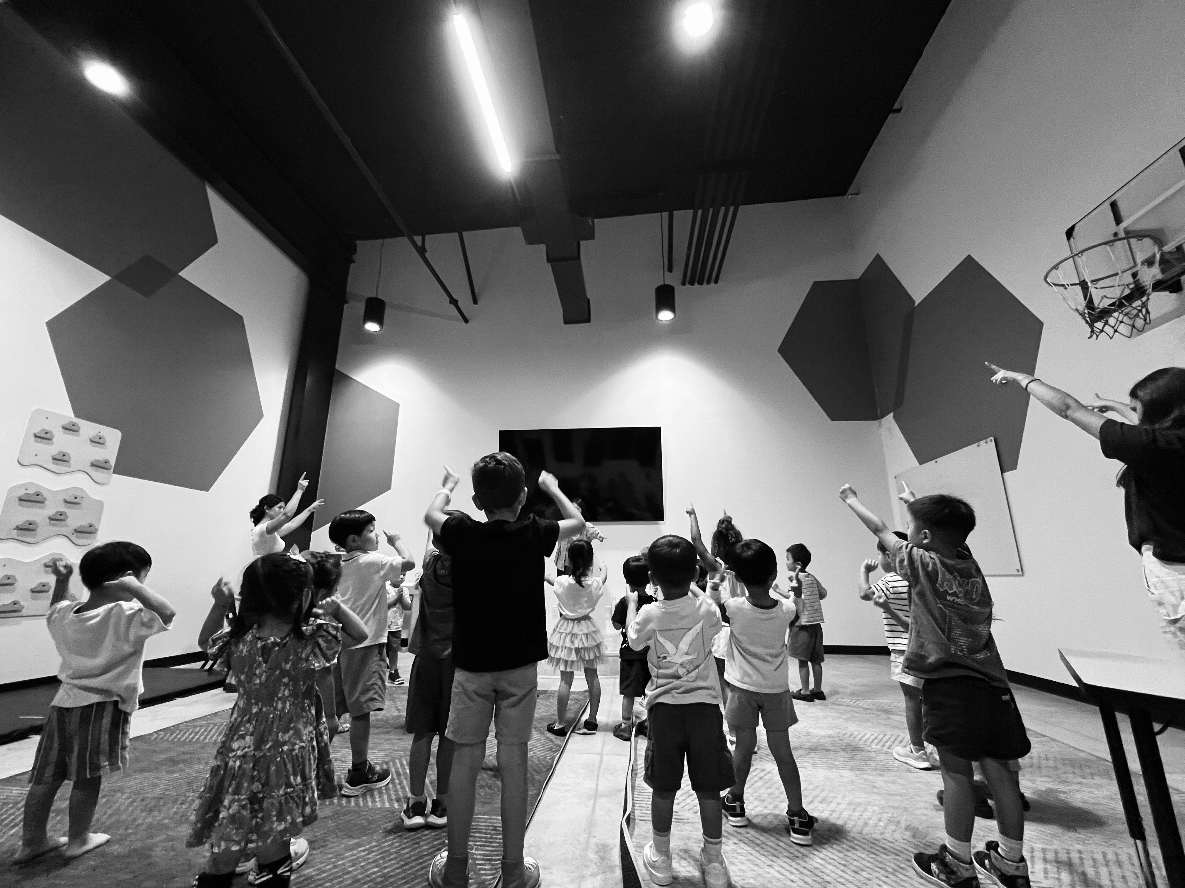 Group of children and adults standing in a room and pointing upward