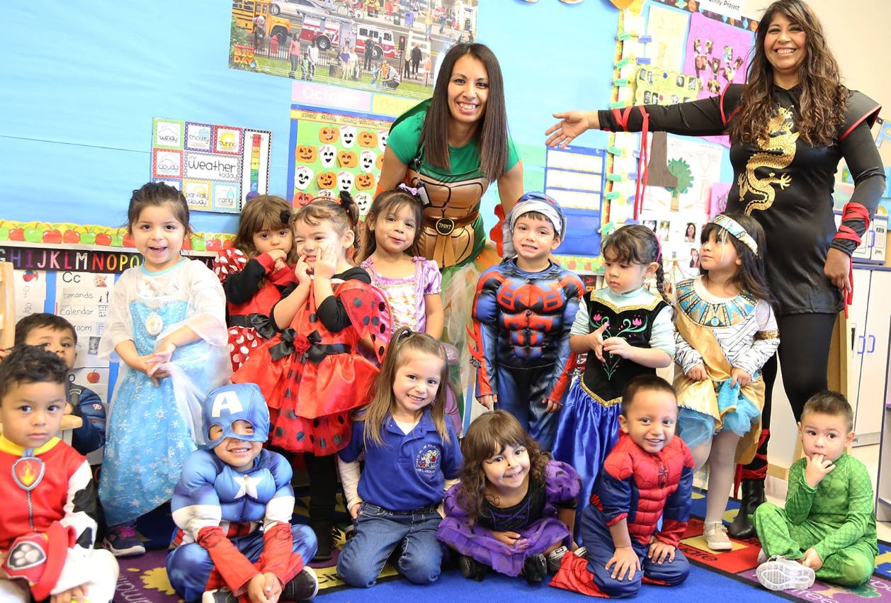 Two adults and many children in costumes in a classroom