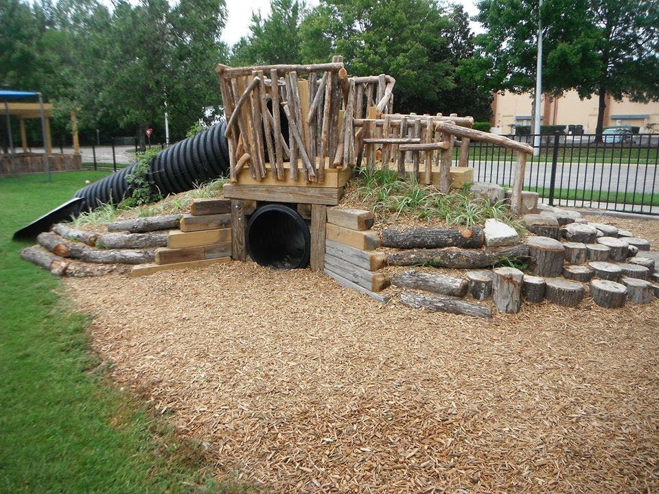 Natural playground structure with wood logs, a tunnel, and a slide