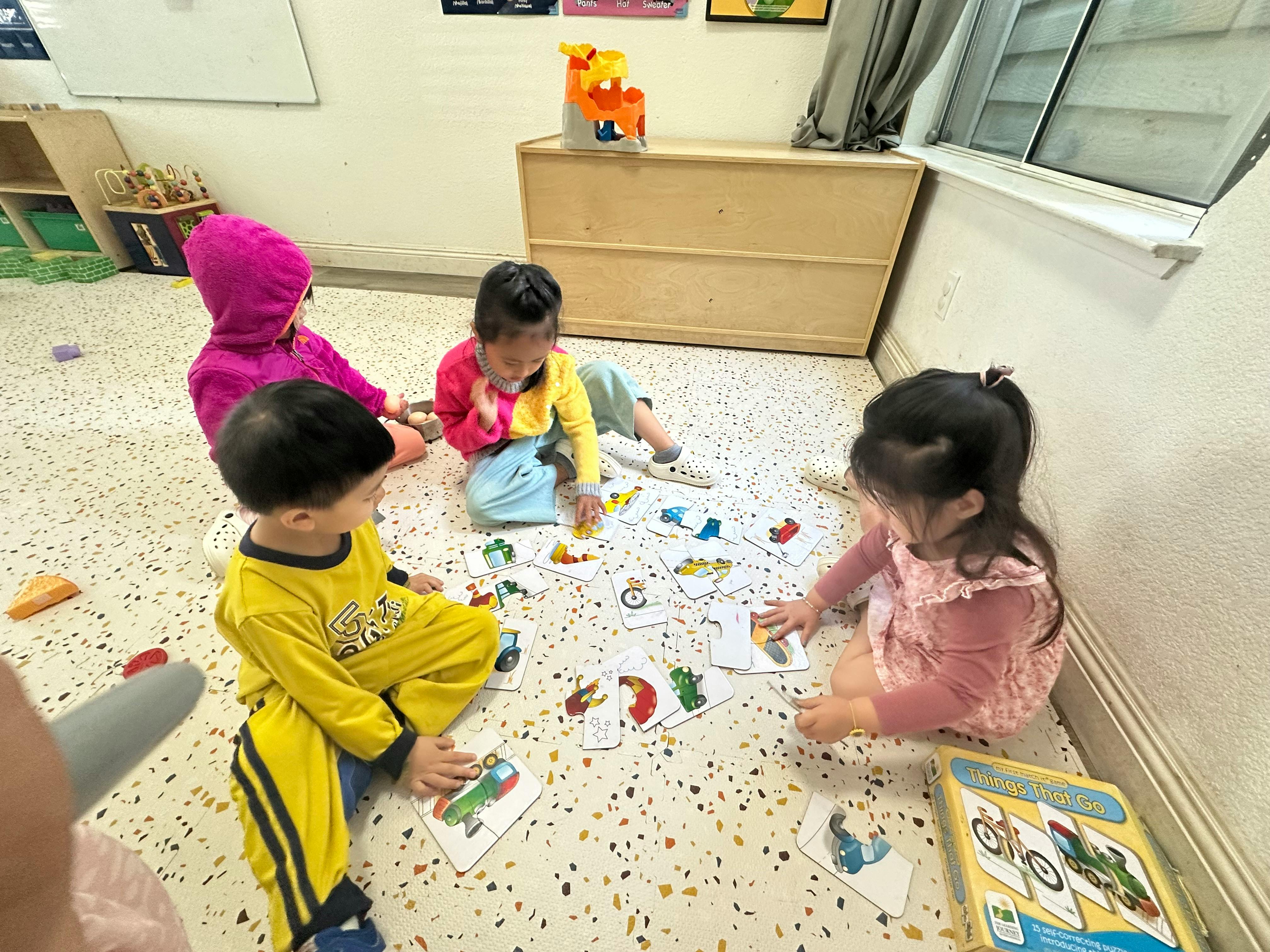Four children playing with cards on the floor in a classroom