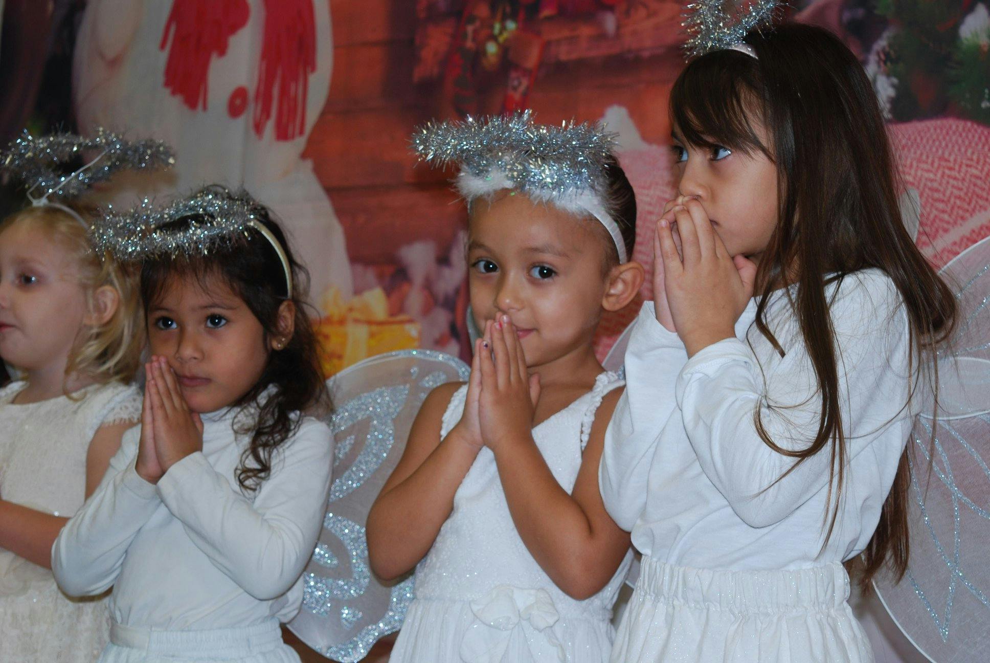 Children in white dresses and halos with hands together