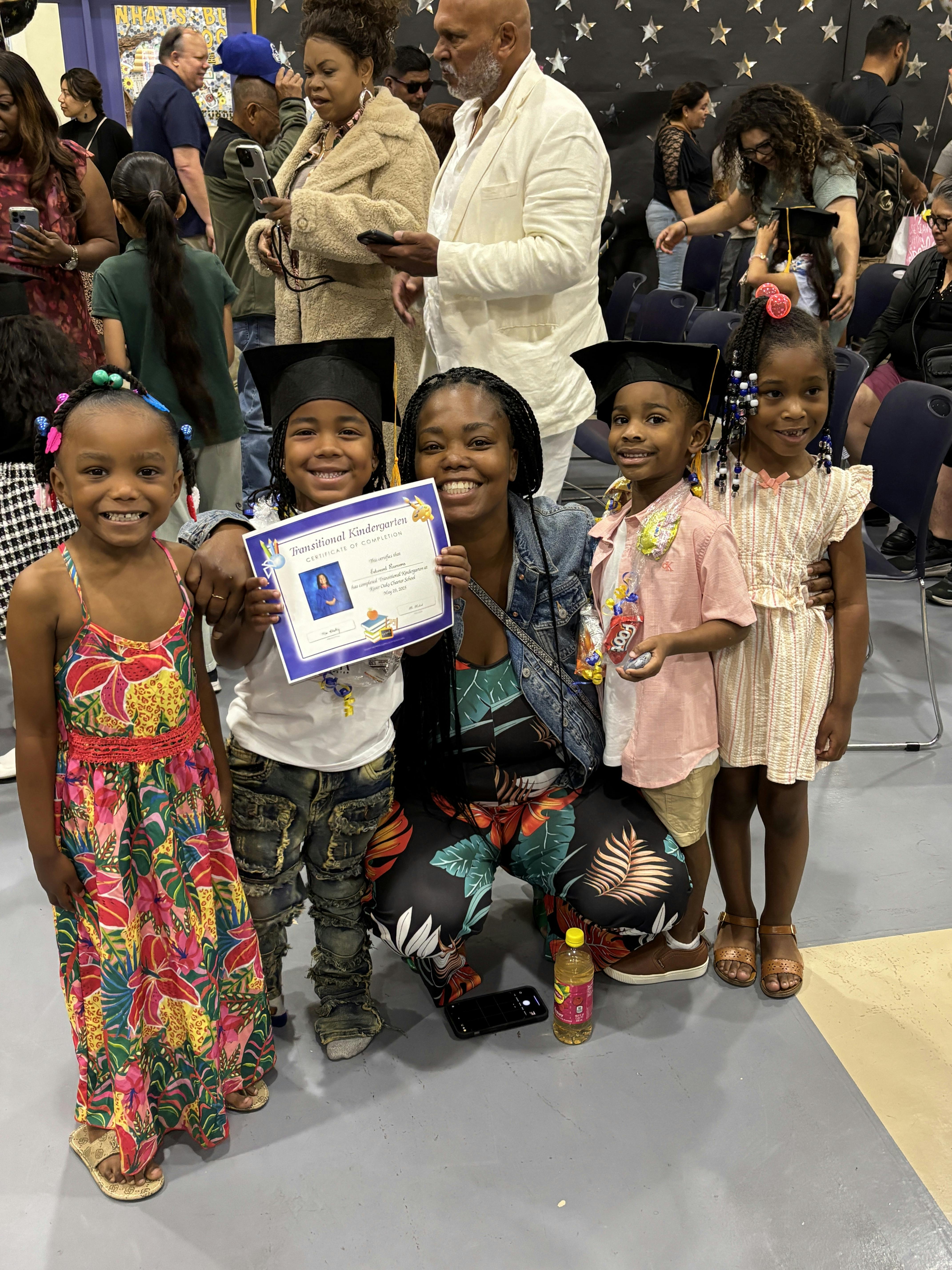 Adult and four children, two in graduation caps, holding a certificate