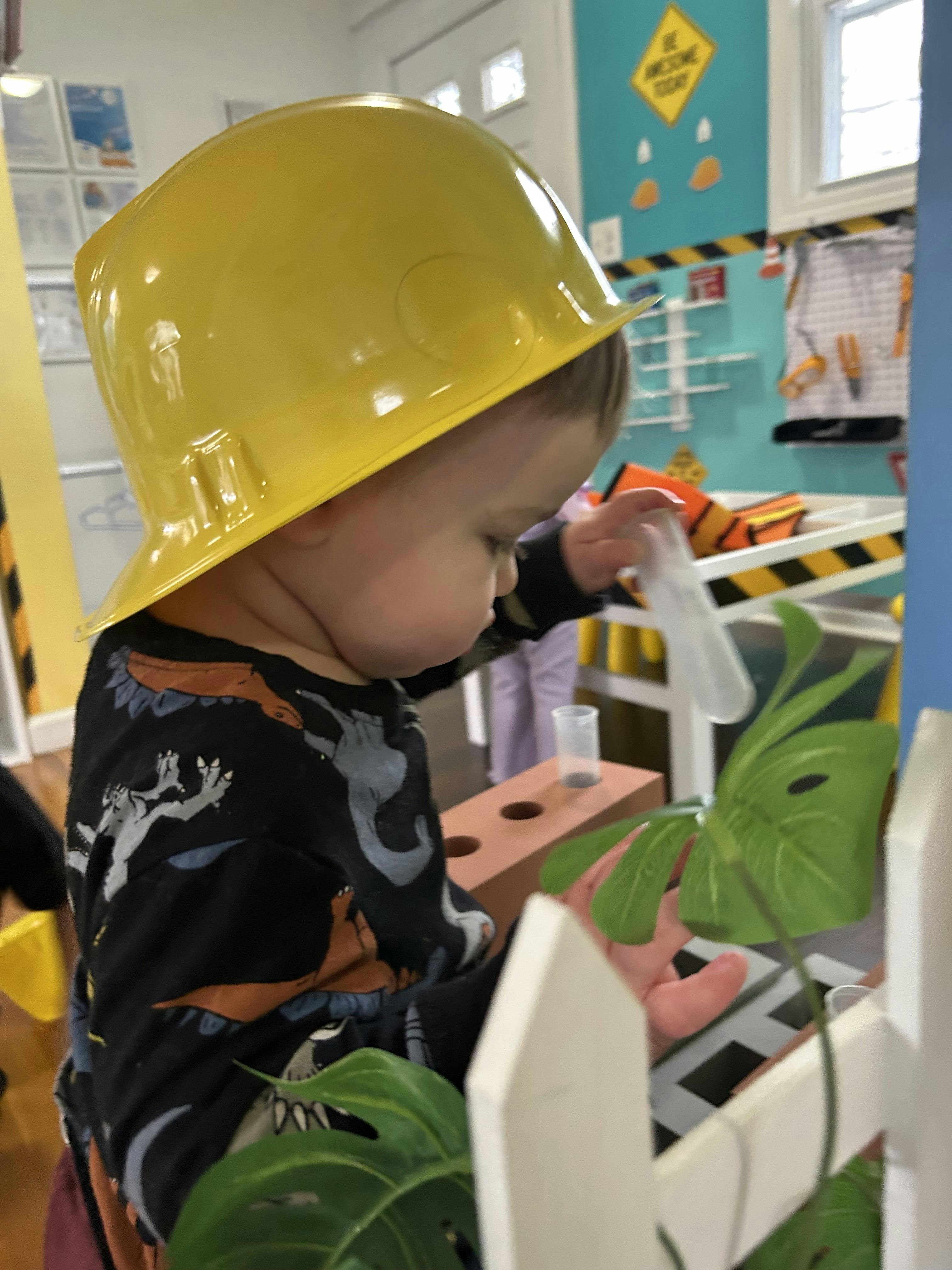 Child in a yellow hard hat holding a clear plastic tube