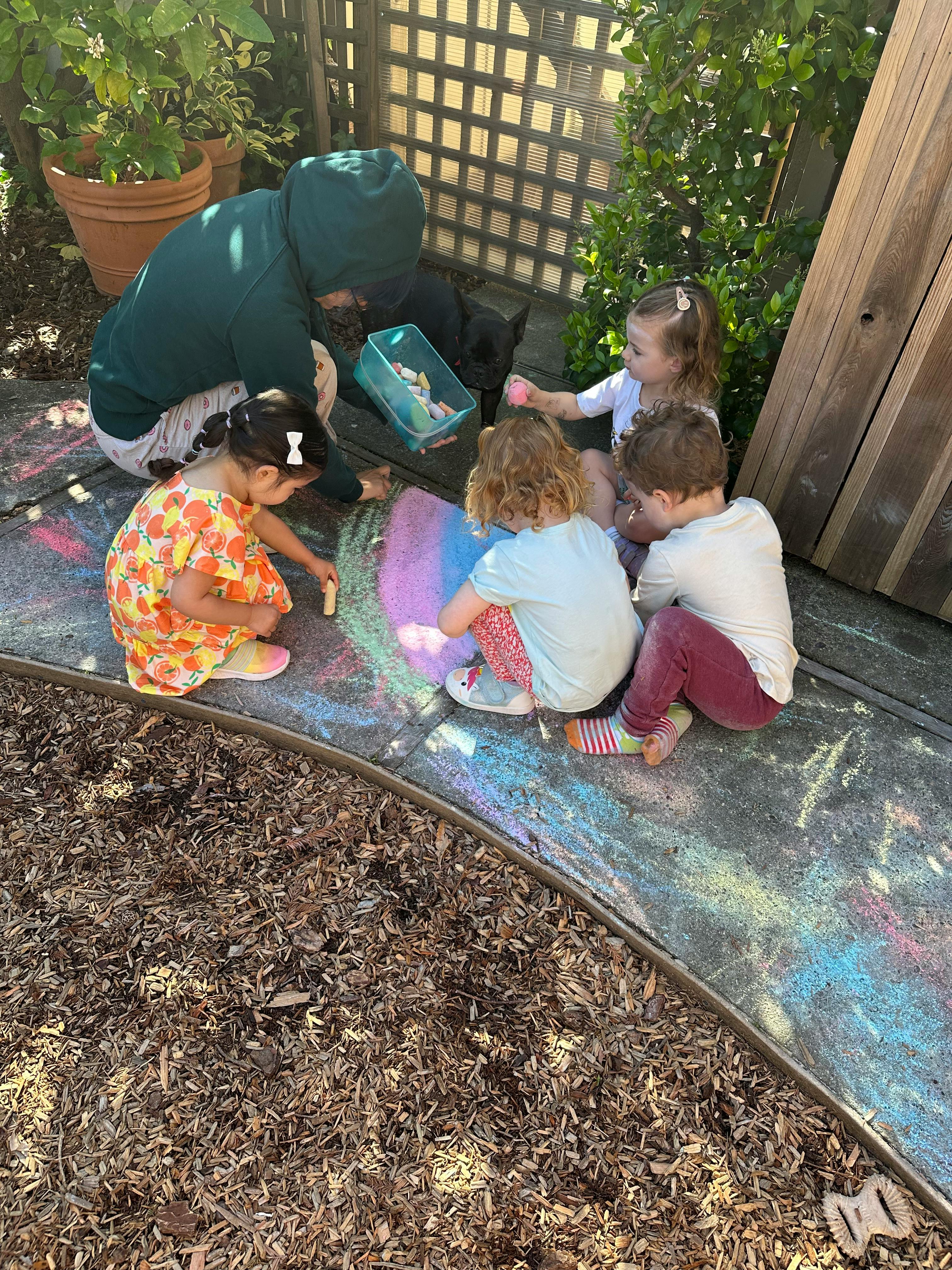 Adult and children drawing with chalk on pavement