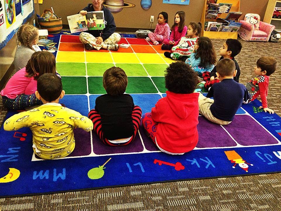 Adult reading a book to a group of children sitting on a colorful rug