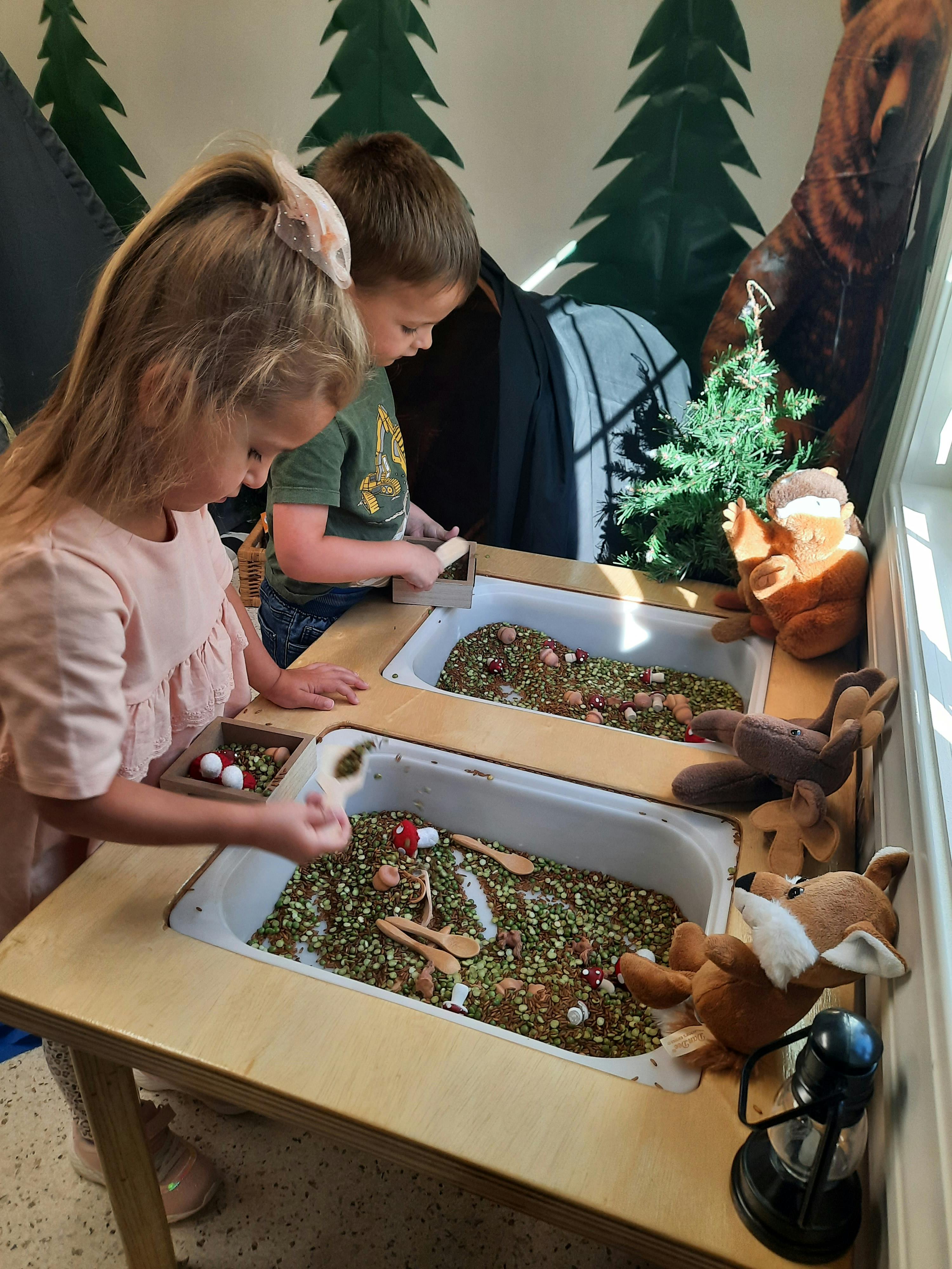 Two children playing with sensory bins filled with split peas
