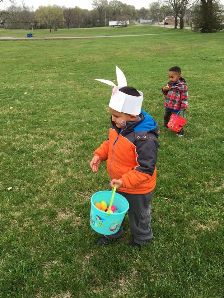 Child in bunny ears holding a basket with eggs, another child in background