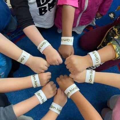 Children forming a circle with their wrists showing I am kind wristbands