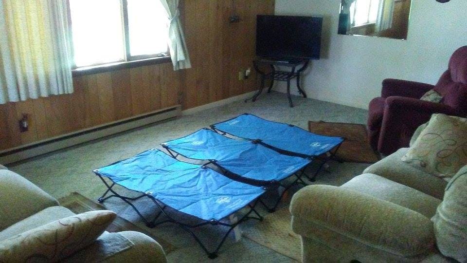 Three blue cots on a carpeted floor in a room with a couch and chairs