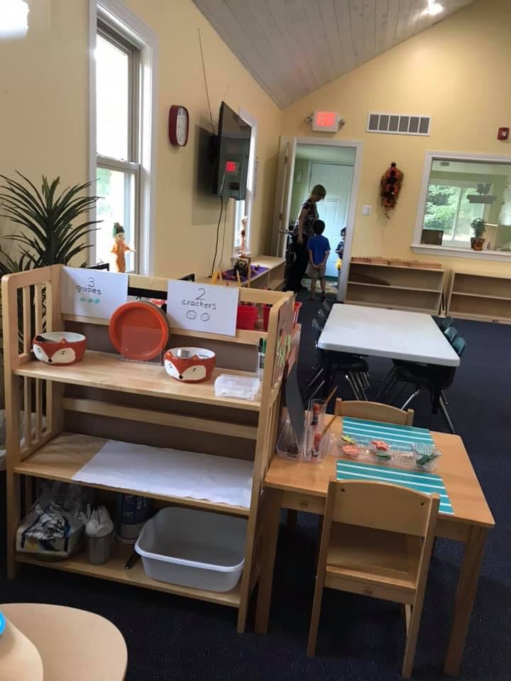 Classroom with shelves, tables, and a person with a child in a doorway