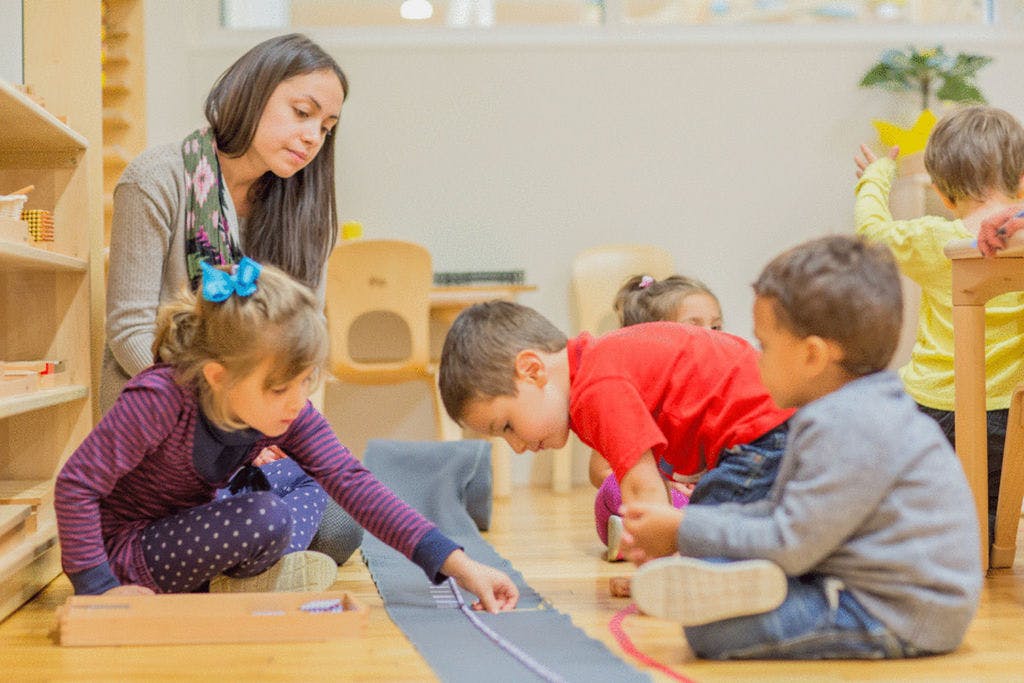 Adult and children on floor playing with learning materials