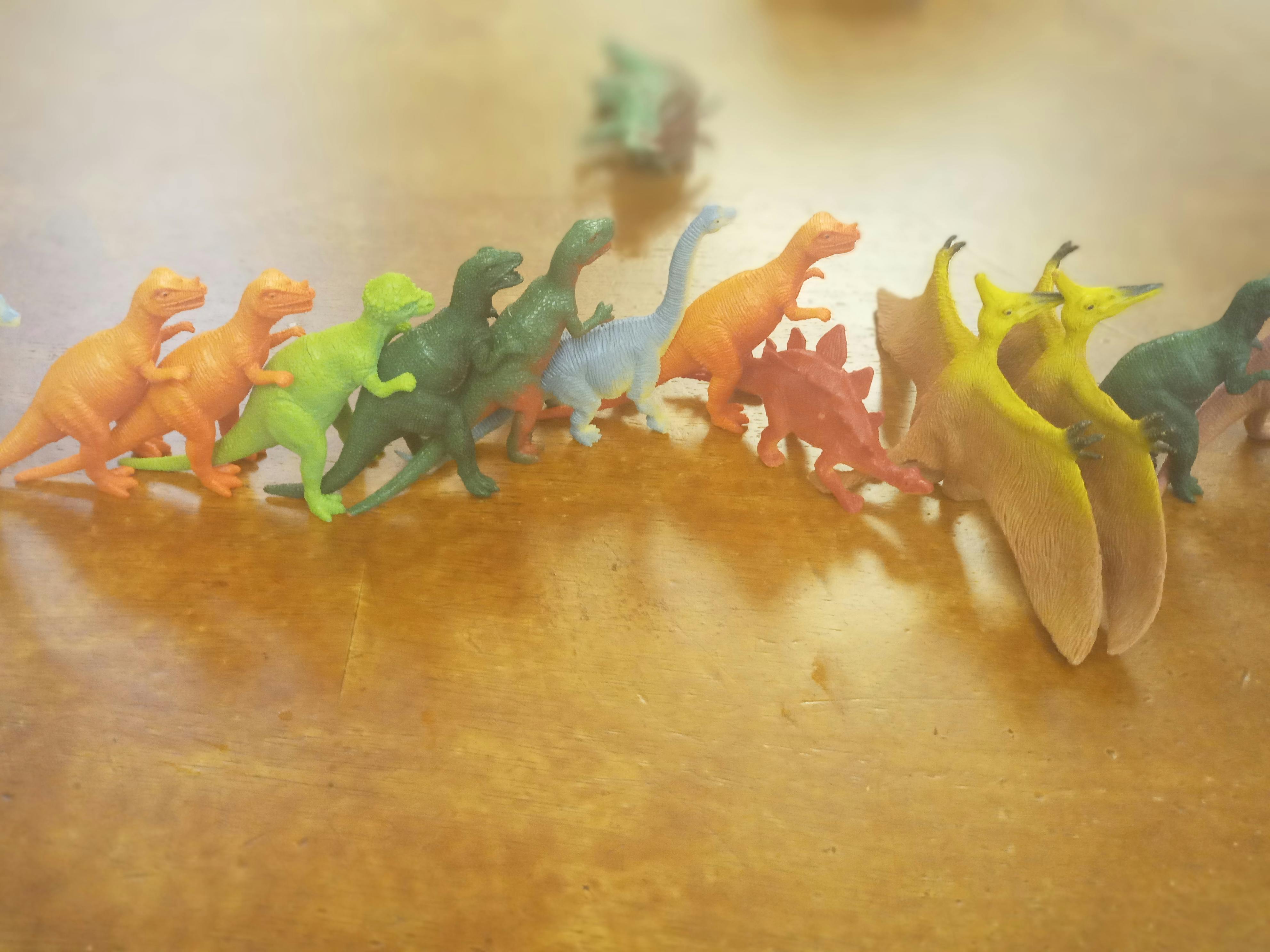 Row of colorful toy dinosaurs on a wooden surface