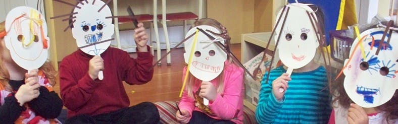 Five children holding up paper masks they created