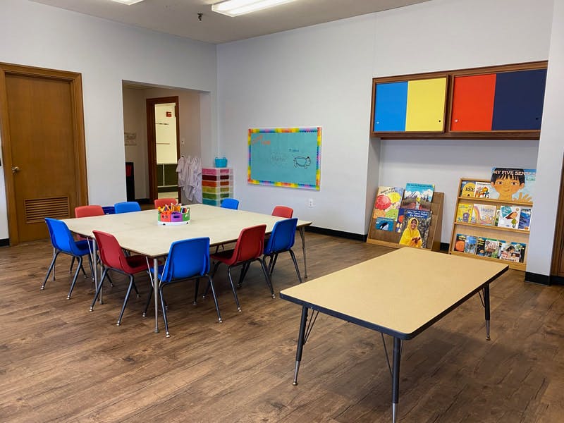 Classroom with tables and chairs, bookshelves, and a bulletin board