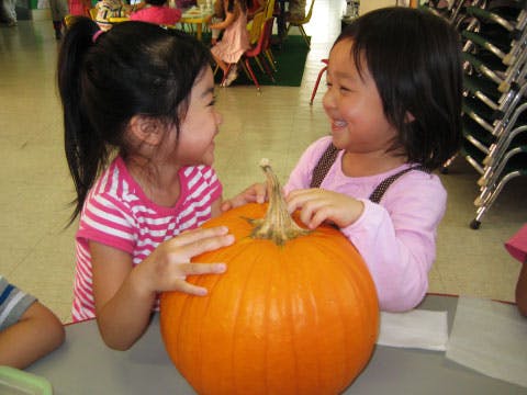 Two children looking at each other over a pumpkin