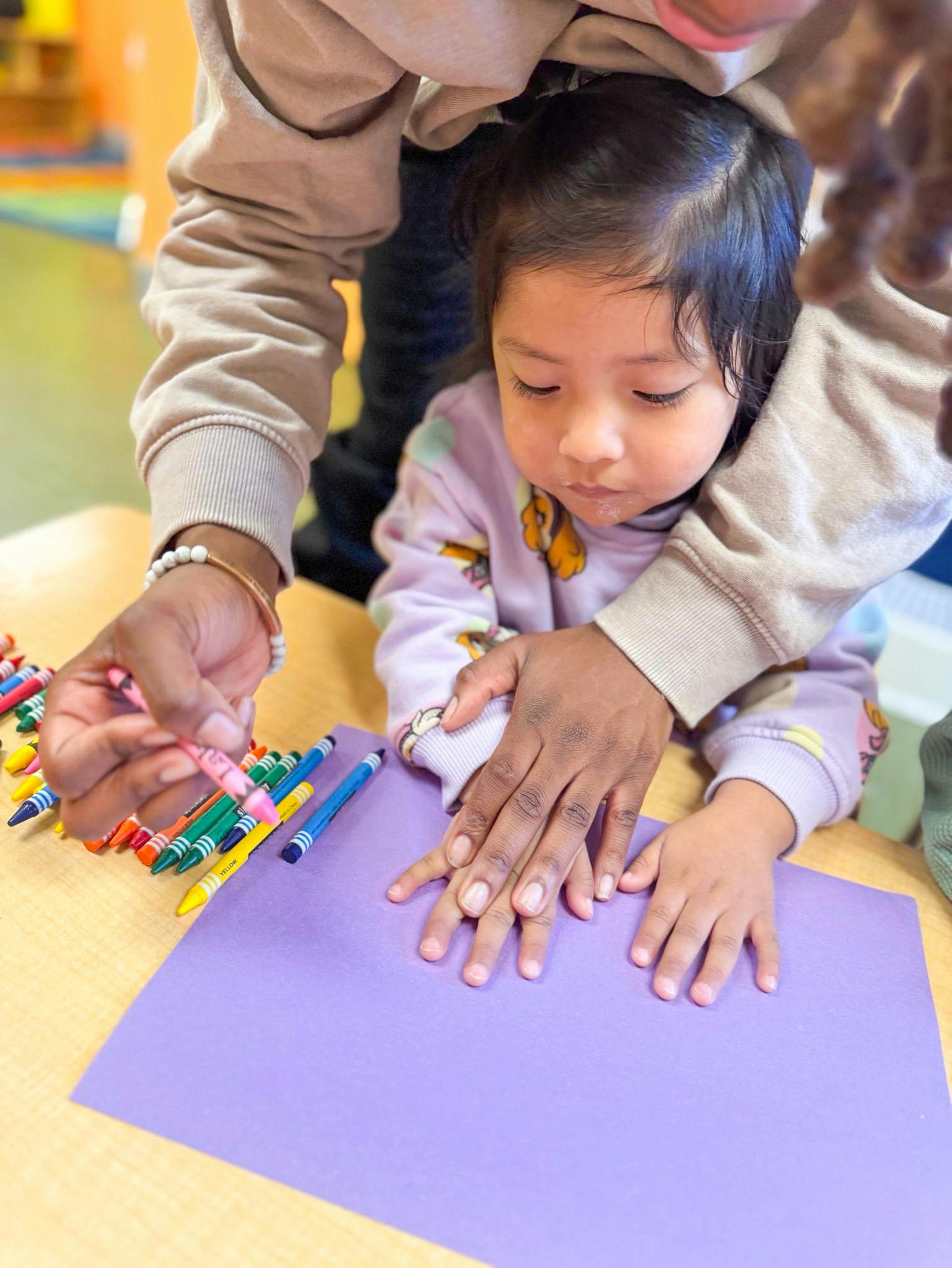 Person helping a child with crayons and purple paper