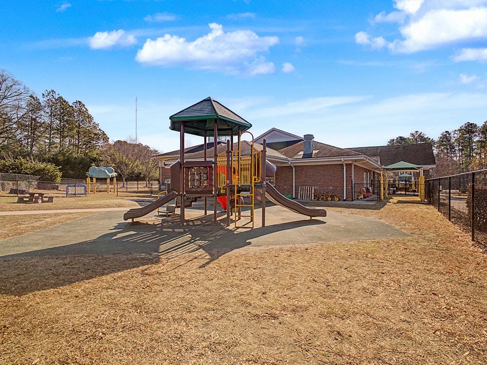 Playground with swings, slides, and a play structure next to a brick building