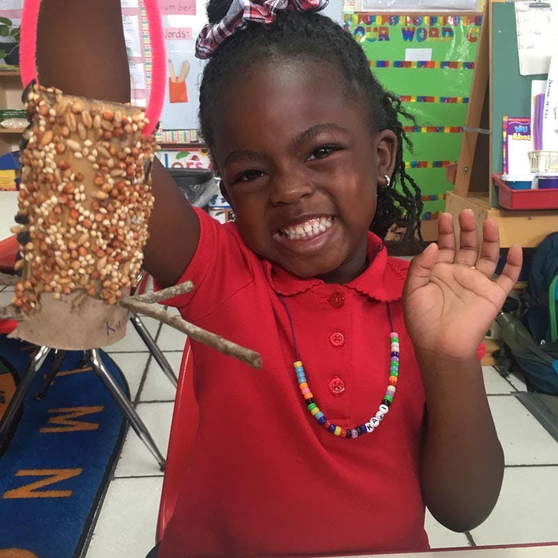Child holding a bird feeder made from a cardboard tube covered in seeds