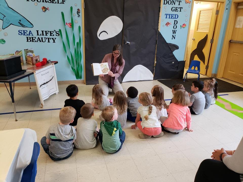 Person reading a book to a group of children sitting on the floor