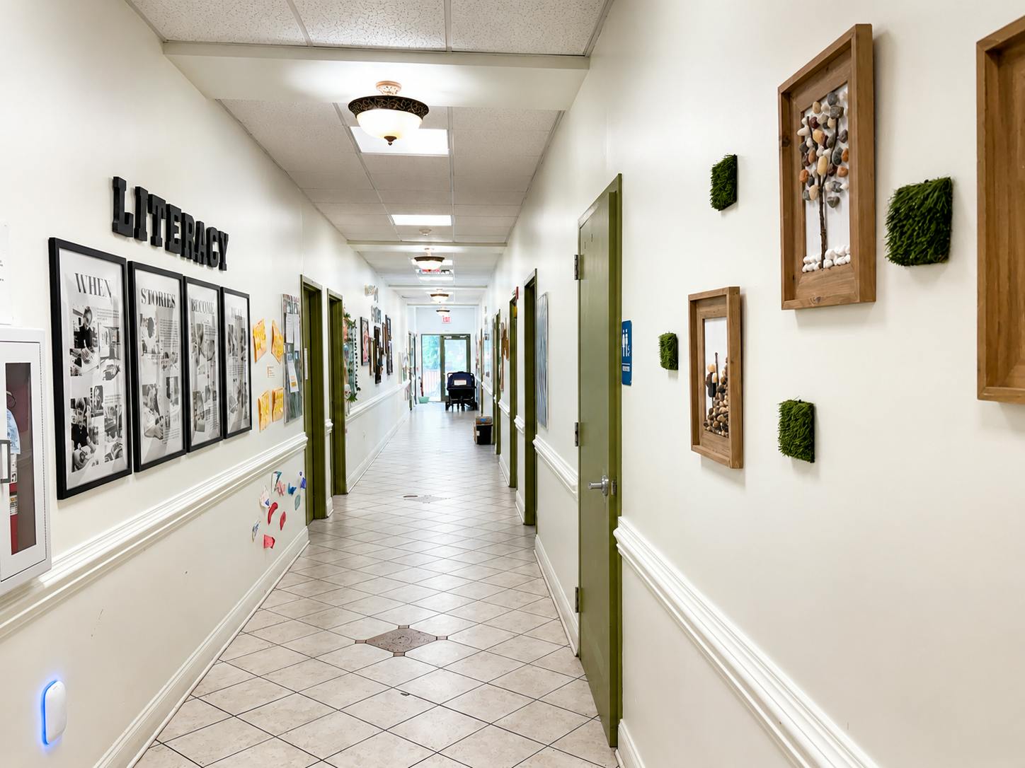 Long hallway with tiled floors, green doors, and literacy-themed wall decor