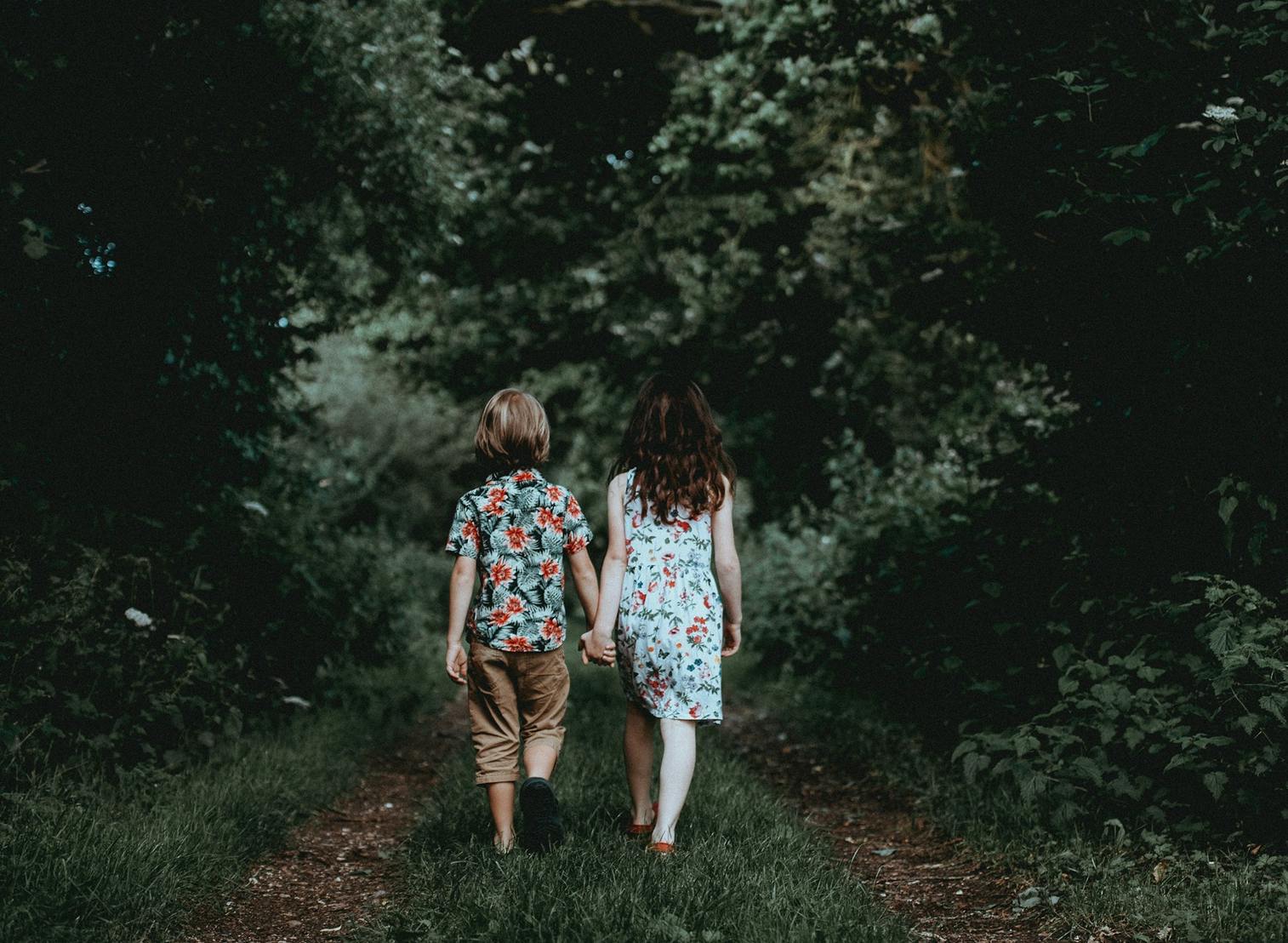 Two children holding hands and walking away on a path
